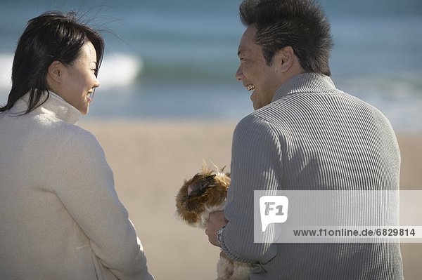 Couple with dog sitting at beach  smiling