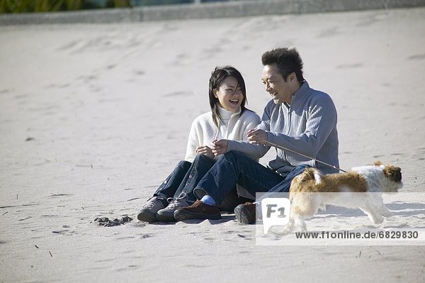 Couple with dog sitting on beach  smiling
