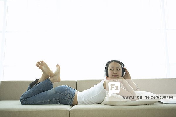 Young Woman Lying on Sofa  Listening to Music
