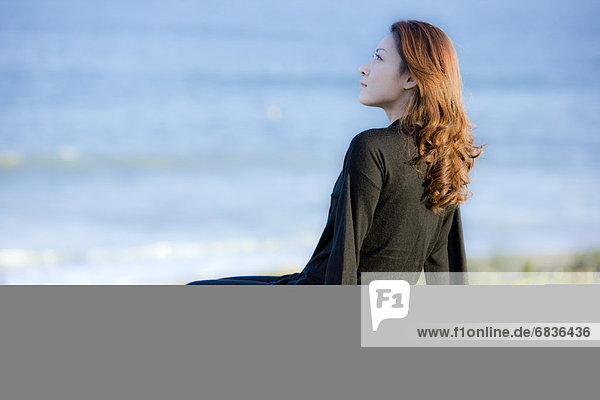 Young woman sitting on beach  looking away