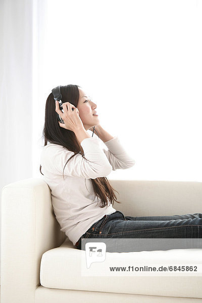 Young Woman Sitting on Sofa  Listening to Music