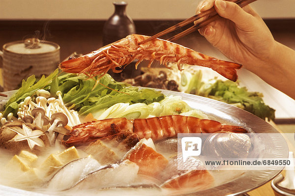 Hand serving seafood from dish with chopsticks