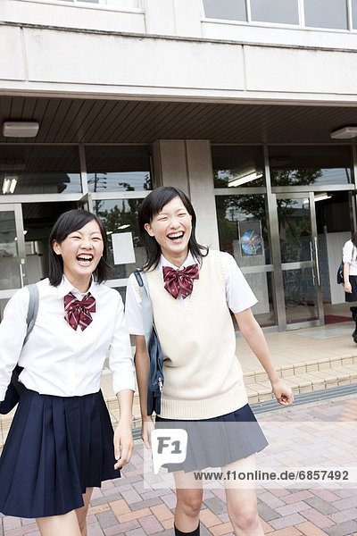 Two Japanese Schoolgirls Leaving School Together and Smiling