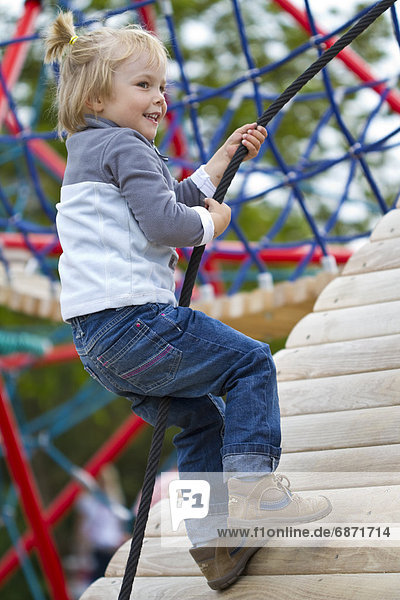 Blondes Mädchen klettert auf einem Spielplatz