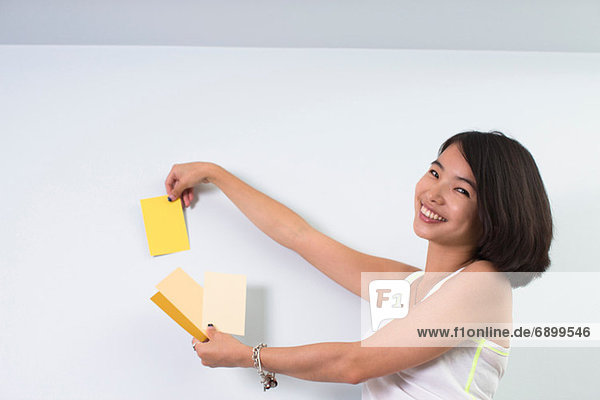 Junge Frau hält Farbmuster an die Wand