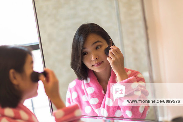Young woman applying makeup using bathroom mirror