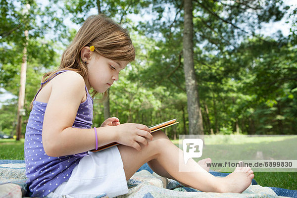 Mädchen sitzend auf Picknickdecke mit digitalem Tablett