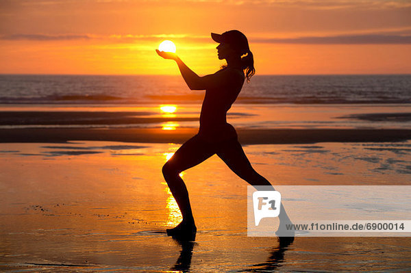 Silhouette einer jungen Frau am Meer bei Sonnenuntergang  die die Sonne hält.