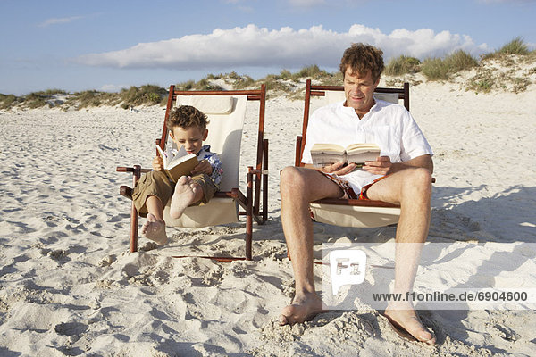 Father and Son Reading on Beach  Majorca  Spain