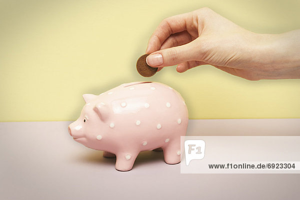 Persons Hand Putting Coin in Piggy Bank