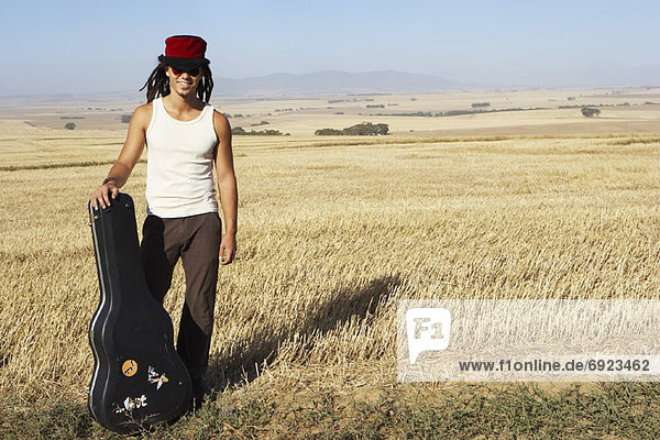Portrait of Man Standing in Field  Holding Guitar Case