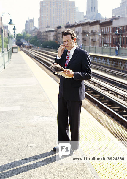 Man with Cellular Phone and Newspaper on Train Platform