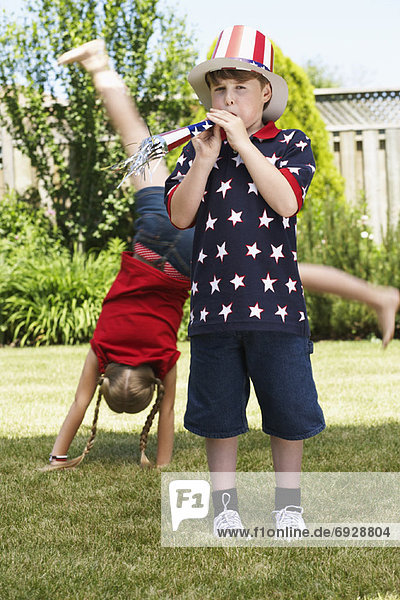 Boy Wearing Stars and Stripes Top and Hat  Girl doing Cartwheel in Background