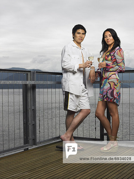 Couple Standing on Deck by Ocean Drinking Wine