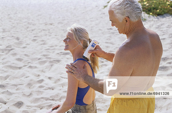 eincremen verteilen Mann Sonnencreme Frau auftragen Paar am Strand