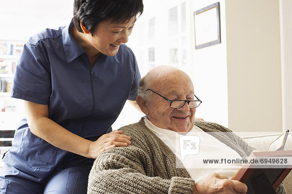 Senior Man Looking at Pictures with Woman Looking over his Shoulder