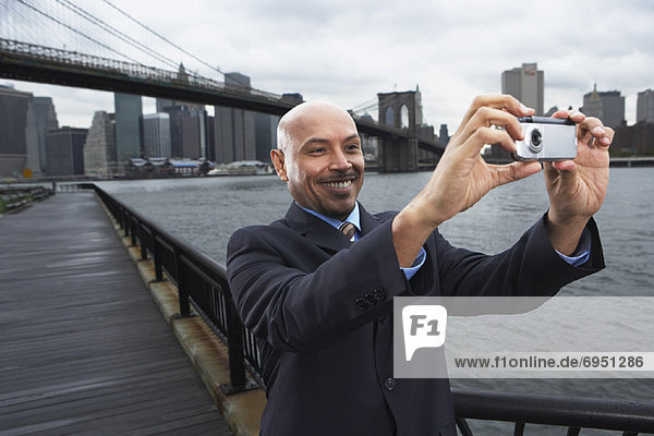 Businessman taking Self Portrait by Brooklyn Bridge  New York City  New York  USA