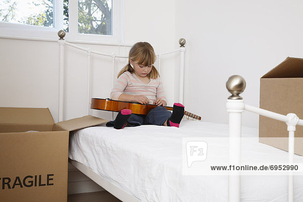 Girl Playing Guitar on Bed with Boxes