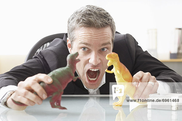 Businessman Playing with Toy Dinosaurs on Desk