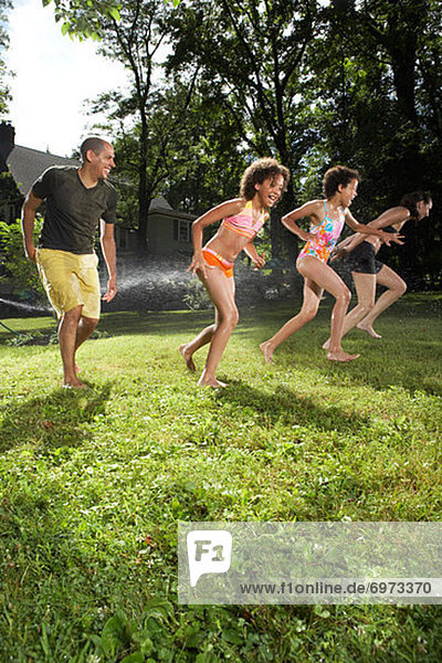 Family Playing in Backyard with Sprinkler