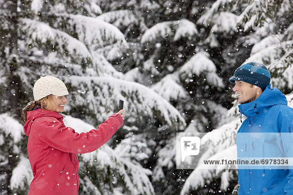 Woman Taking Picture of Man with Camera Phone Outdoors in Winter  Whistler  British Columbia  Canada