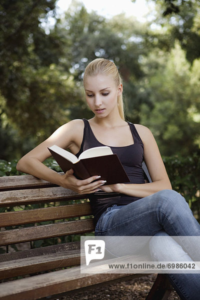 Young Woman Sitting on Park Bench Reading a Book