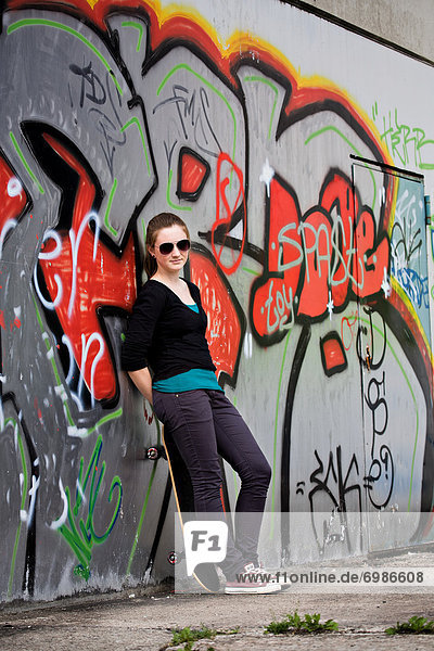 Teenage girl with skateboard standing in front of a graffiti wall  urban area