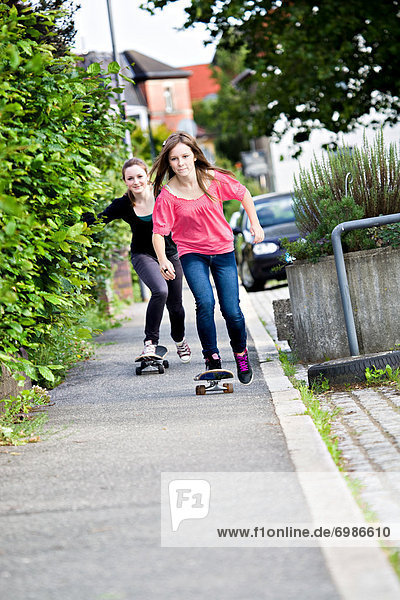 Two teenage girls skateboarding on a pavement