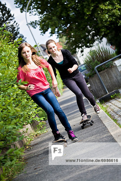 Zwei Mädchen  Teenager fahren Skateboard auf Bürgersteig
