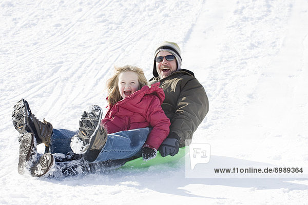 Father and Daughter Sledding in Winter
