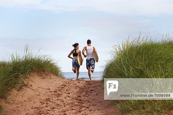 Young Woman and Young Man holding Skimboards while Running to Beach  PEI  Canada