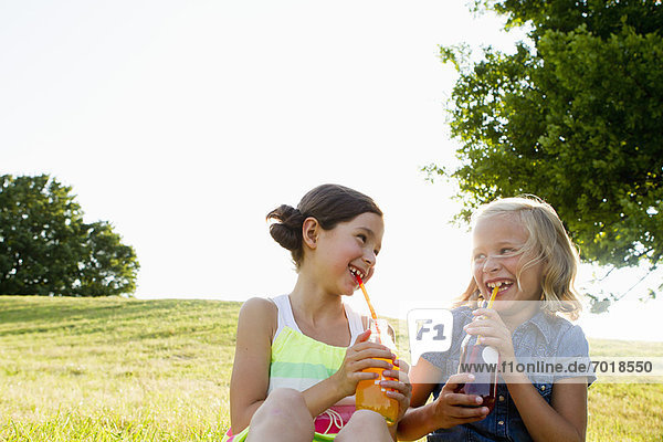Lachende Mädchen trinken Saft im Freien