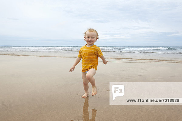 Junge geht in Wellen am Strand spazieren