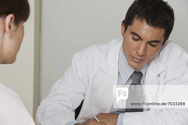 Doctor sitting across from female patient  writing prescription