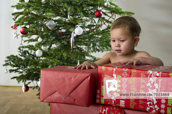 Baby Mädchen berührt gestapelte Weihnachtsgeschenke