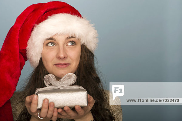 Junge Frau mit Weihnachtsgeschenk  in Gedanken aufblickend