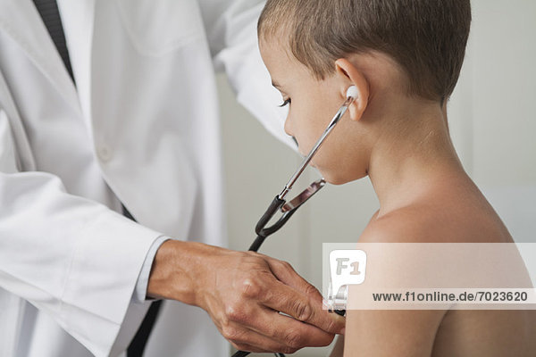 Arzt lässt Jungen mit Stethoskop auf die eigene Brust hören