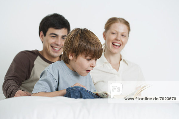 Boy reading book with parents