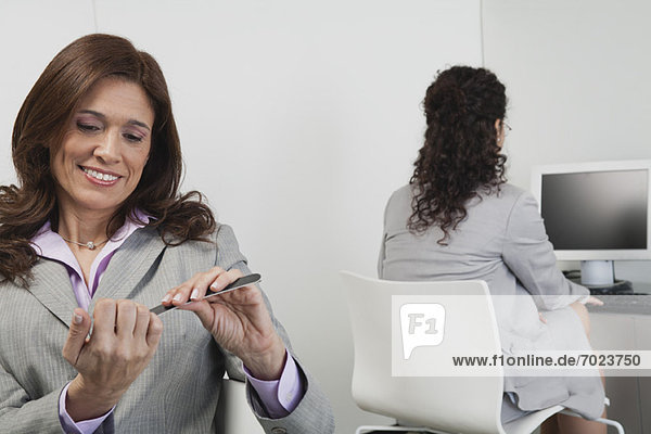 Woman filing her nails in office  colleague working in background