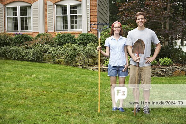 Young couple with rake and spade in garden