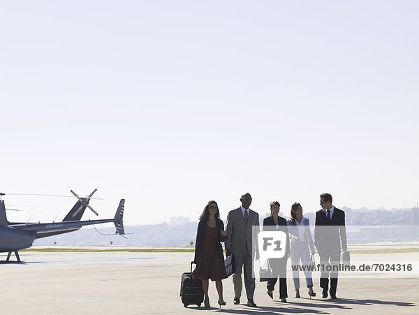Group of businesspeople walking on runway near helicopter