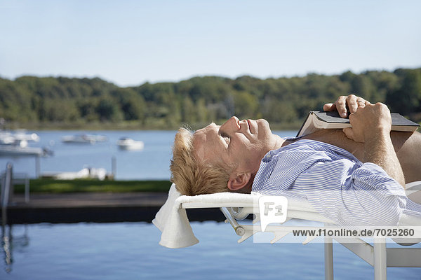 Man lying on lounge chair  book on chest