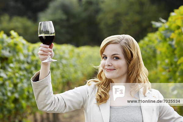 Young woman holding glass of red wine in vineyard (portrait)