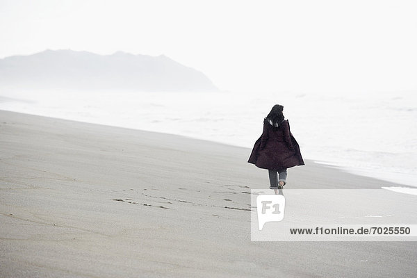 Woman walking on sandy beach (rear view)