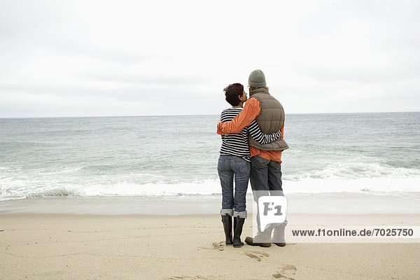 Couple standing on beach and looking at ocean