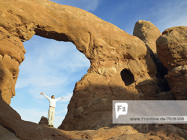 Man standing under arched rock with arms raised