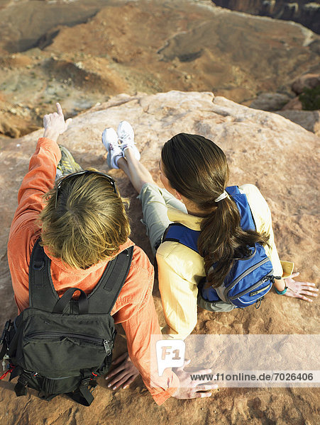 Young couple with backpacks sitting on rock  high angle view  rear view
