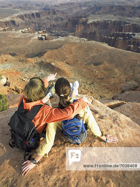 Young couple with backpacks looking at rock strata on cliff