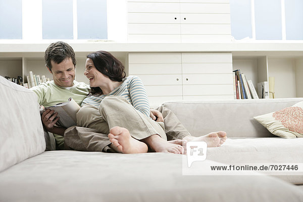 Mid adult couple reading magazine on sofa