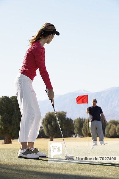 Woman playing golf  man holding golf flag